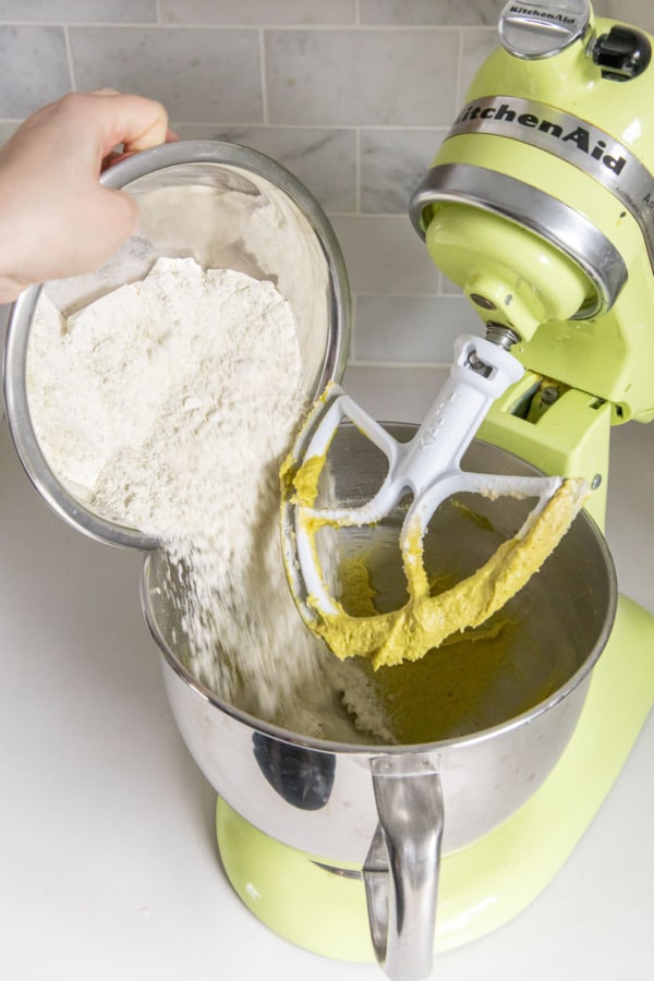 Adding dry flour mixture to mixing bowl of green electric mixer.