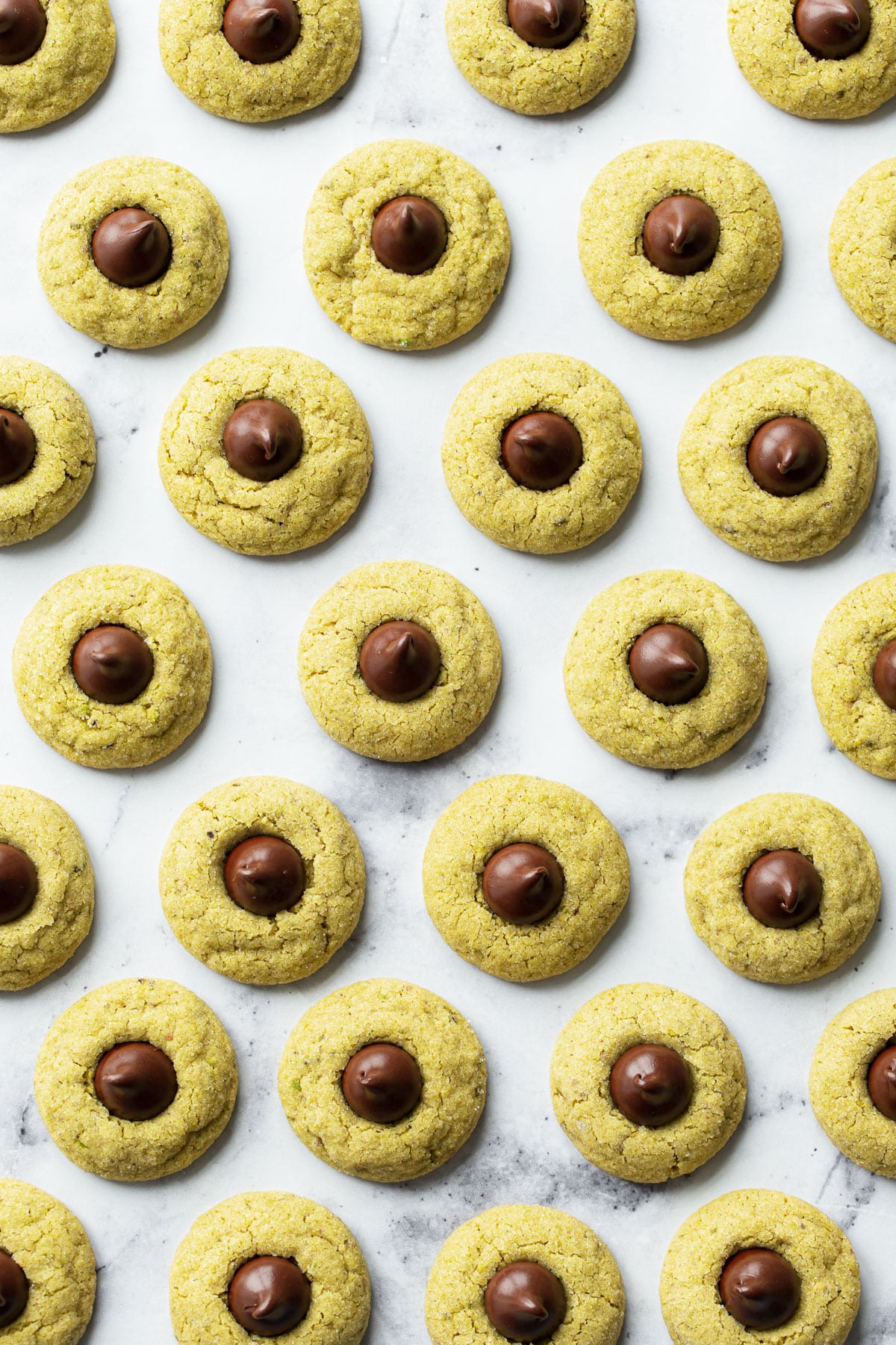 Overhead, staggered rows of Pistachio Butter Blossom Cookies with dark chocolate kisses.