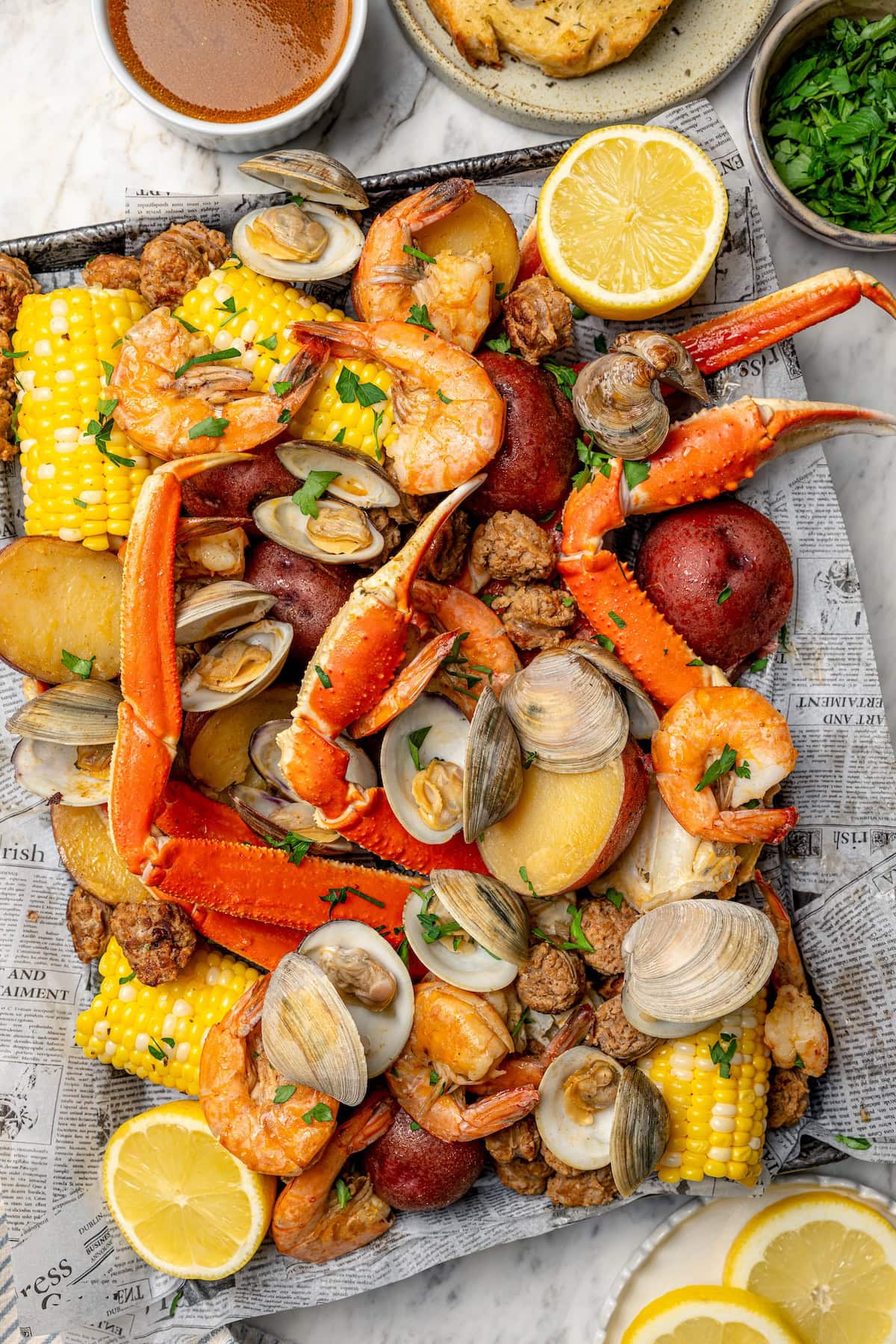 With spicy chorizo, potatoes, corn, crab, clams and shrimp, this seafood boil recipe is a complete meal in one pot. So easy to make too! Overhead view of seafood boil arranged on newspaper-lined sheet pan
