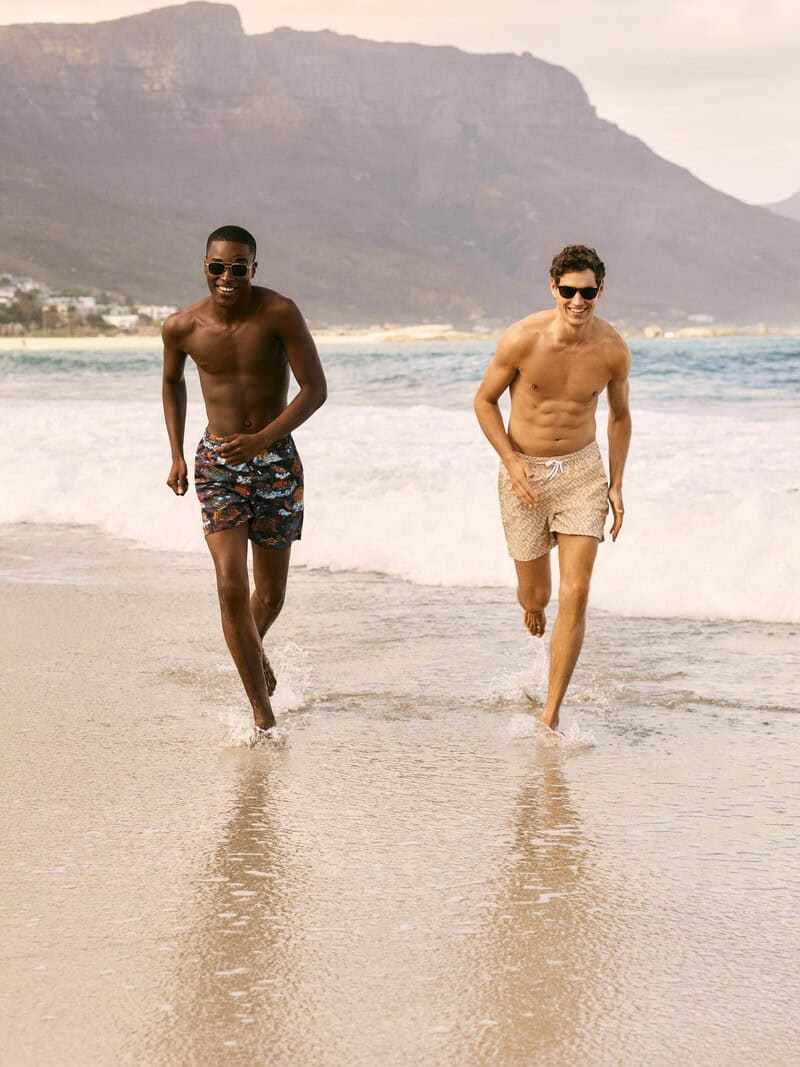 Two Men running on the beach wearing swim shorts