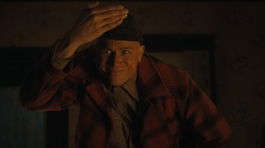 Monster: The Ed Gein Story stars Charlie Hunnam as the actor playing Ed Gein, shown here smiling in the dark with his hand above his face