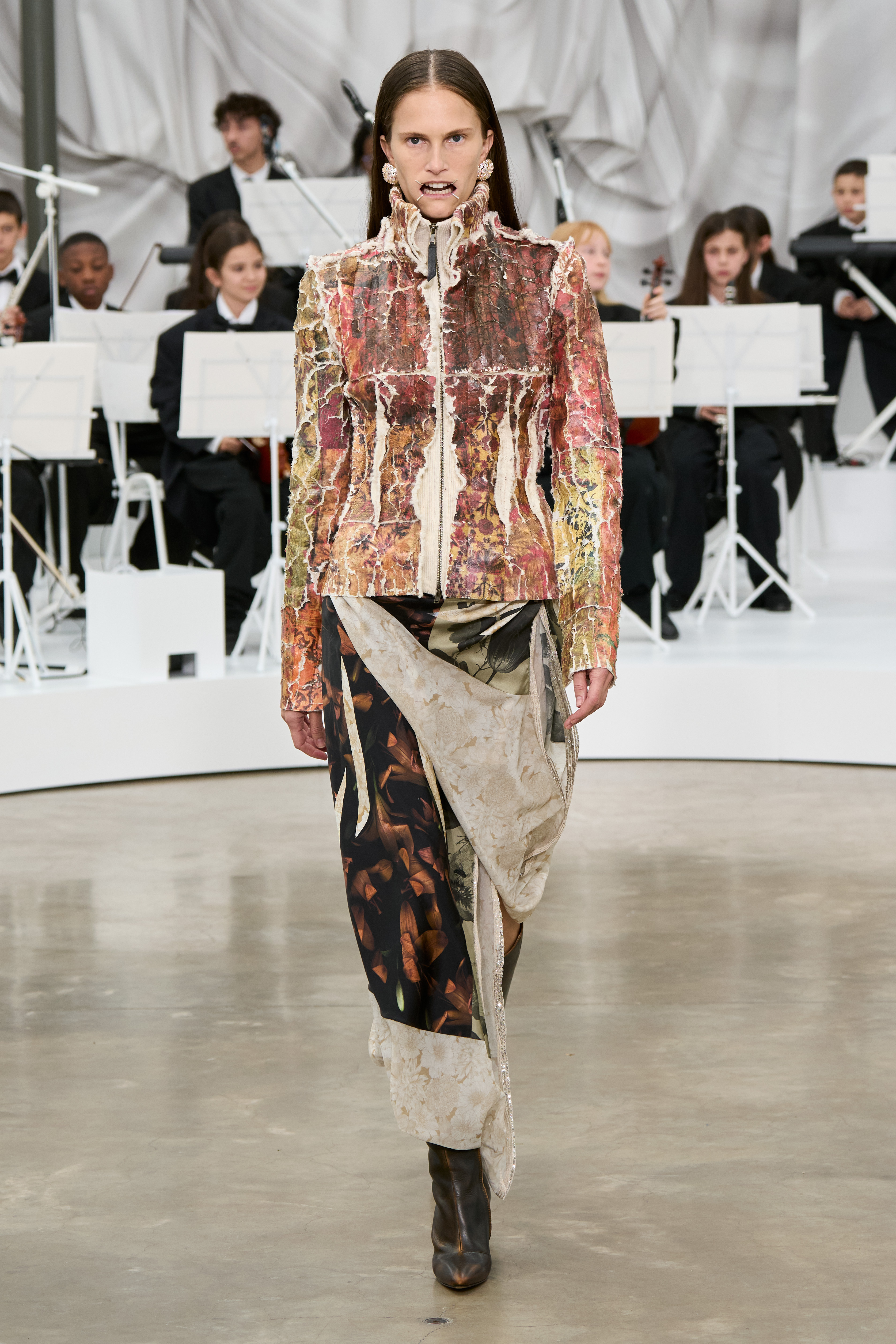 A model at the S/S 26 Maison Margiela show wearing a printed jacket and skirt with boots.
